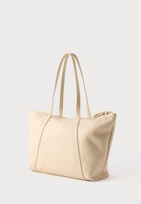 Μπεζ δερμάτινη τσάντα tote με δύο μακριές λαβές και κλείσιμο με φερμουάρ, εμφανιζόμενη πάνω σε λευκό απλό φόντο.