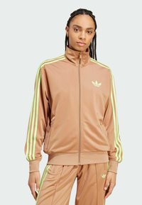 Braune Trainingsjacke aus glattem Material mit grünen Streifen an den Ärmeln. Mit hohem Kragen und durchgehendem Reißverschluss. Das Adidas-Logo ist sichtbar.