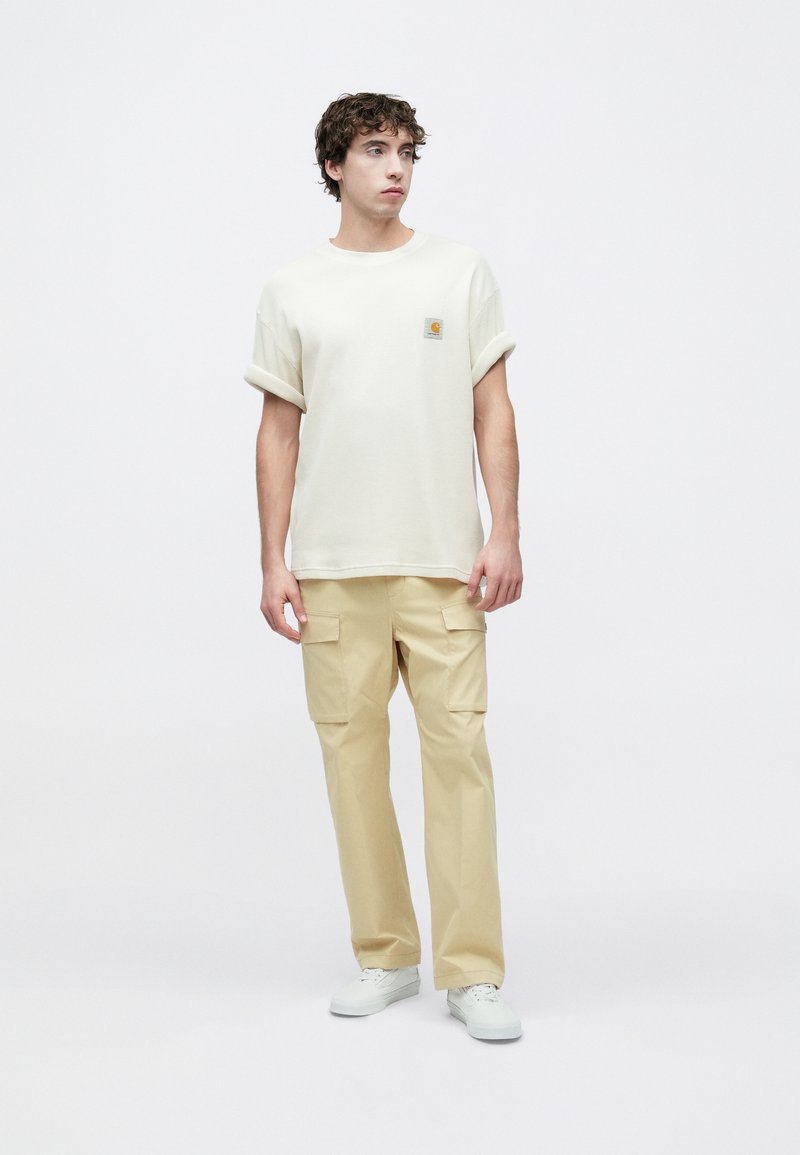 Light beige textured t-shirt with rolled sleeves and a small logo patch. Paired with light khaki cargo pants featuring side pockets.