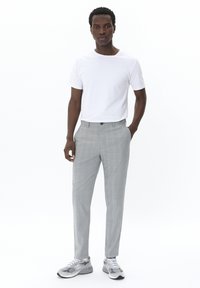Pantalones de cuadros grises con un corte ajustado, combinados con una camiseta blanca de cuello redondo y zapatillas grises, de pie contra un fondo blanco.