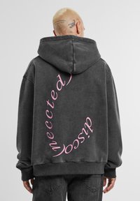 Dunkelgrauer Hoodie mit einem großen gebogenen, rosa Textdesign auf dem Rücken. Er hat eine Kapuze, lange Ärmel und einen lässigen Schnitt.