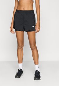 Schwarze Sportshorts mit elastischem Bund, die ein weißes Adidas-Logo an der Seite und ein Innenfutter haben. Kombiniert mit schwarzen Sportschuhen.