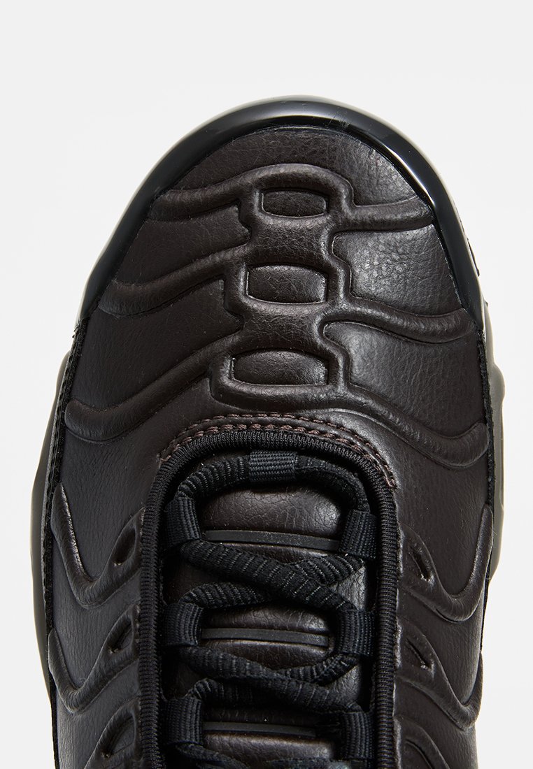 Zapatillas de cuero marrón con superposiciones de textura ondulada, una puntera de goma negra y cordones negros con un patrón circular en la parte superior.