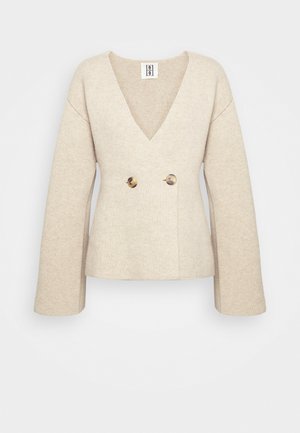 Beige knitted sweater with a deep V-neck, long sleeves, and a fitted waist featuring two large round buttons at the front.