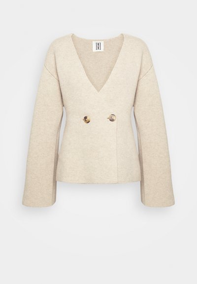 Maglione beige lavorato a maglia con profondo scollo a V, maniche lunghe e vita aderente, impreziosito da due grandi bottoni rotondi sul davanti.