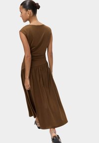 Brązowa sukienka bez rękawów z dopasowanym gorsetem i zwiewną, marszczoną spódnicą. Gładka tkanina i skromny okrągły dekolt.