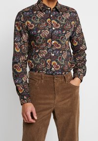 Pitkähihainen paita tummasta kankaasta, jossa on värikäs paisley-kuvio vihreän, punaisen ja sinisen sävyissä; yhdistetty ruskeisiin samettihousuihin.