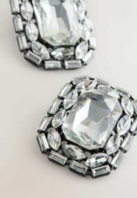 Rechteckige, klare Kristallbroschen mit mehreren kleineren ovalen und rechteckigen Kristallen in schwarzer Fassung auf hellem Untergrund.