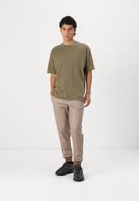 Oliven grøn bomulds t-shirt med rund hals, parret med beige mønstrede sweatpants og sorte træningssko med teksturerede såler.