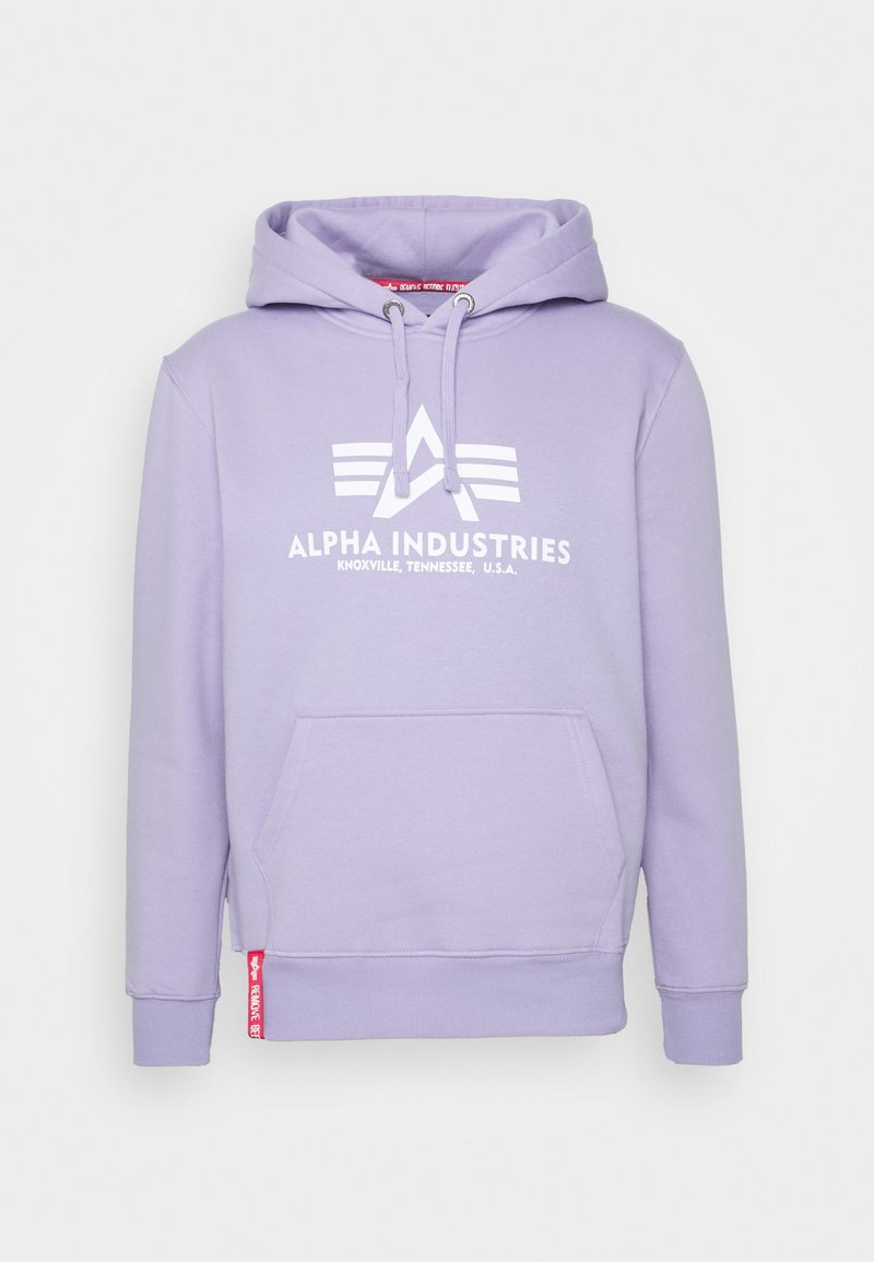 Levanduľová mikina s kapucňou a predným vreckom, biele logo a text Alpha Industries, kapucňa so šnúrkou a malá červená nášivka na spodnom okraji.