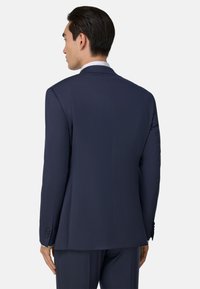 Jūrinis švarkas iš lygaus audinio, pritaikytas pagal figūrą. Turi vieną ventiliaciją, įpjautas apykakles ir sagčių rankoves. Galiniame vaizde matyti švarios linijos ir be siūlių dizainas.