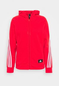 Sudadera roja con capucha y cierre de cremallera, hecha de una tela suave. Presenta un diseño de tres rayas blancas en las mangas y un parche negro con el logo de Adidas.