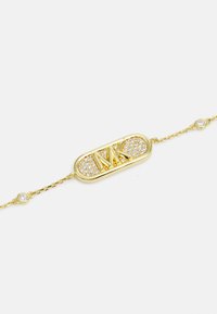 Bracciale in oro con un pendente ovale con il logo "MK", impreziosito da piccoli cristalli trasparenti, e una delicata catena con accenti circolari.
