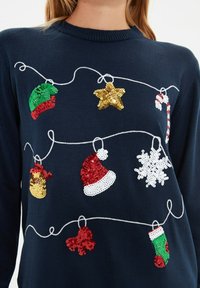 Navy blauer Pullover mit Pailletten-Dekorationen: grüne und rote Handschuhe, goldener Stern, Zuckerstange, roter Weihnachtsmann-Hut, Schneeflocke und grüner Strumpf.