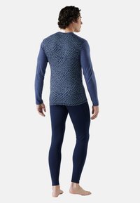 Langarm basislaag top in blauw met abstract marinepatroon, gecombineerd met donkerblauwe leggins, gemaakt van rekbare stof. Met voet en een strakke pasvorm.