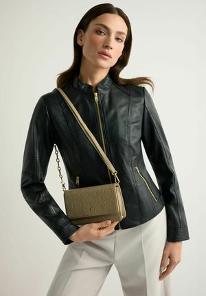 Kobieta w czarnej skórzanej kurtce i jasnych spodniach, trzyma beżową pikowaną torbę na ramię ze złotymi elementami.