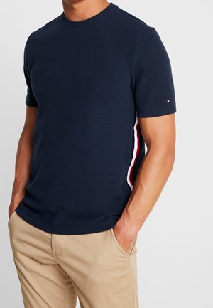 Marineblaue T-Shirt mit kurzen Ärmeln aus strukturiertem Stoff, mit weißen und roten Seitenstreifen, rundem Ausschnitt und figurbetontem Schnitt.