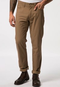 Beige Baumwollhose mit geradem Bein, ausgestattet mit Seitentaschen und umgeschlagenen Säumen, kombiniert mit dunkelbraunen Schnürstiefeln.