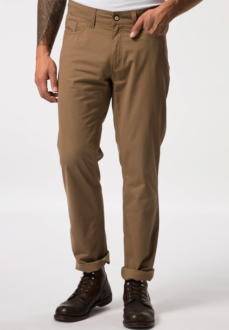 Beige Baumwollhose mit geradem Bein, ausgestattet mit Seitentaschen und umgeschlagenen Säumen, kombiniert mit dunkelbraunen Schnürstiefeln.