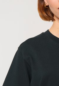 T-shirt en coton noir avec un col rond et des manches courtes, possédant une texture lisse et un design épuré. Boucle d'oreille en or visible.