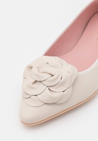 Chaussure plate beige à bout pointu avec intérieur rose et grande décoration fleur en cuir plié sur le dessus.
