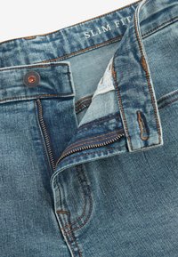Uske slim fit traperice u srednje plavoj boji. Imaju kontrastne narančaste šavove, zatvarač i metalnu kopču.