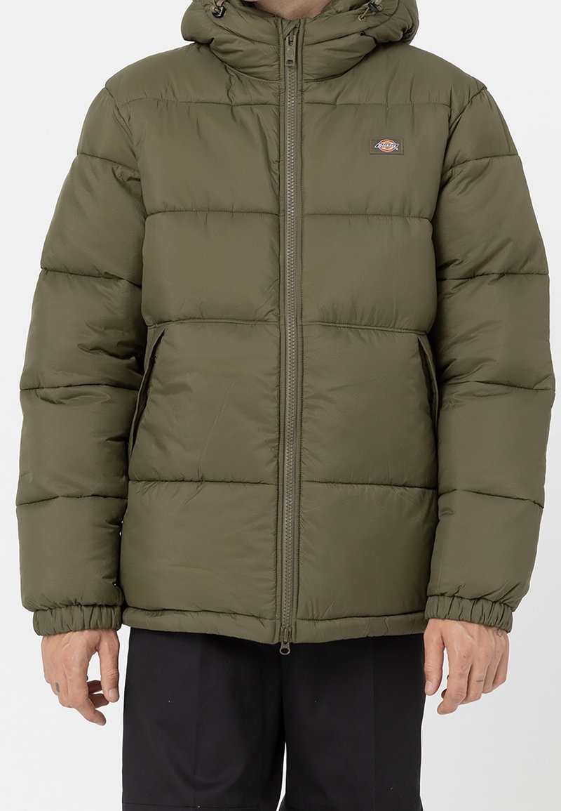 Kurtka puchowa koloru oliwkowo-zielonego z zamkiem z przodu, kapturem i elastycznymi mankietami. Charakterystyczny przeszywany wzór i logo na lewej piersi.