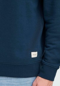 Sudadera navy hecha de un tejido suave y texturizado con un cuello y puños acanalados. Presenta una pequeña etiqueta de marca en el dobladillo.