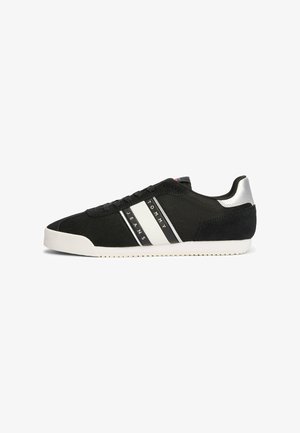 Schwarzer Sneaker aus Mesh- und Wildledermaterial, mit weißen und schwarzen Streifen, strukturiertem Obermaterial, flacher Sohle und silbernem Akzent an der Ferse.