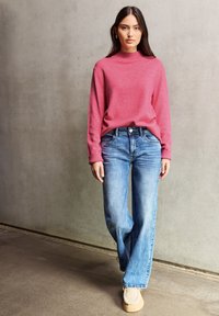 Maglione a collo alto rosa chiaro con maniche lunghe abbinato a jeans a vita alta blu chiaro a palazzo. Maglia tessuta e vestibilità casual.