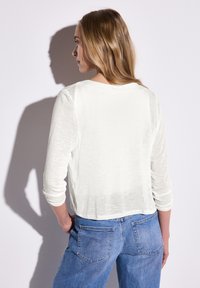 Vit, lättviktig långärmad topp med avslappnad passform, rund halsringning och cropped nederkant. Matchad med blå denimjeans med bakfickor.