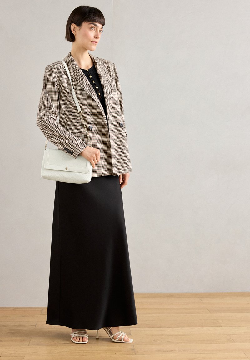 Blazer de cuadros de doble botonadura, vestido negro, bolso de bandolera blanco y tacones con tiras. Paleta de colores neutros en general con texturas distintas.