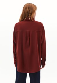 Camicia a maniche lunghe in tessuto rosso scuro, con cucitura a yoke sul retro e vestibilità morbida. Include polsini con bottoni e orlo curvo.