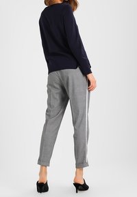 Námořnický svetr, šedé vzorované kalhoty s úzkým střihem, s bočními pruhy, a černé lodičky na vysokém podpatku. Jemná textura, neformální styl.