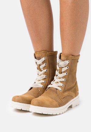 Bottines en cuir tan avec un design perforé, lacets blancs et semelle blanche. Présente un capuchon lisse et des détails cousus.