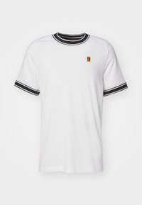 T-shirt blanc à manches courtes avec col et poignets rayés noirs. Affiche un petit logo coloré sur la poitrine. Fabriqué en tissu en maille.