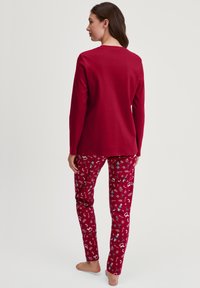 Rode lange mouwen top gecombineerd met rode geblokte broek met witte en blauwe feestelijke ontwerpen. Zachte stof met een relaxte pasvorm.