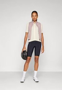 Kerékpáros öltözet világos lila mellénnyel, krémszínű mezben, fekete rövidnadrággal és fehér zoknival. Kiegészítők között fekete bukósisak is található.