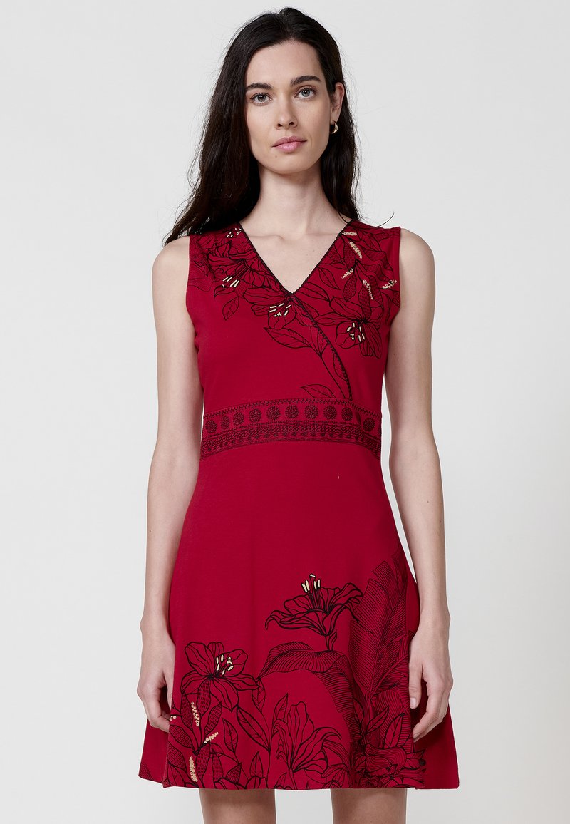 Rotes ärmelloses Kleid mit V-Ausschnitt, verziert mit schwarzer floraler Stickerei und einem Akzent an der Taille. Ausgestellte Silhouette mit glatter Textur.