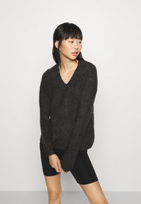 Dunkelgrauer, gestrickter V-Ausschnitt-Pullover mit langen Ärmeln und lockerer Passform, kombiniert mit schwarzen Radhosen; strukturierter Stoff mit einem schlichten Design.