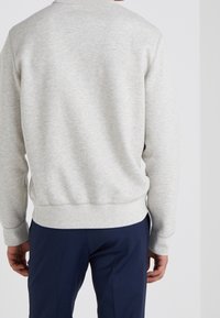 Světle šedá mikina se žebrovanými manžetami a lemem, vyrobená z měkké látky, v kombinaci s tmavě navy kalhotami, které vykazují uvolněný střih a jednoduchý design.