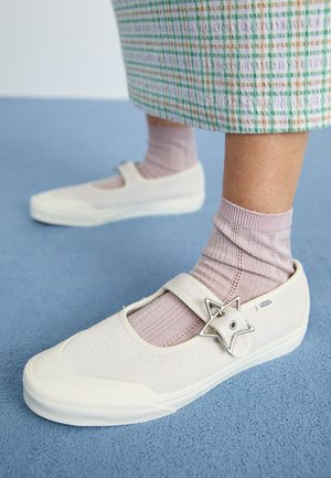 Baltos kanvas batai su zomšiniu viršumi, dirželis per pėdą ir sidabrinė žvaigždute akcentas. Derinami su šviesiai rožinėmis raukšlėtomis kojinėmis.