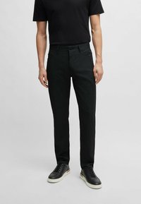 Pantalon slim noir en tissu texturé, doté de poches traditionnelles, d'une fermeture à bouton et associé à des baskets noires.