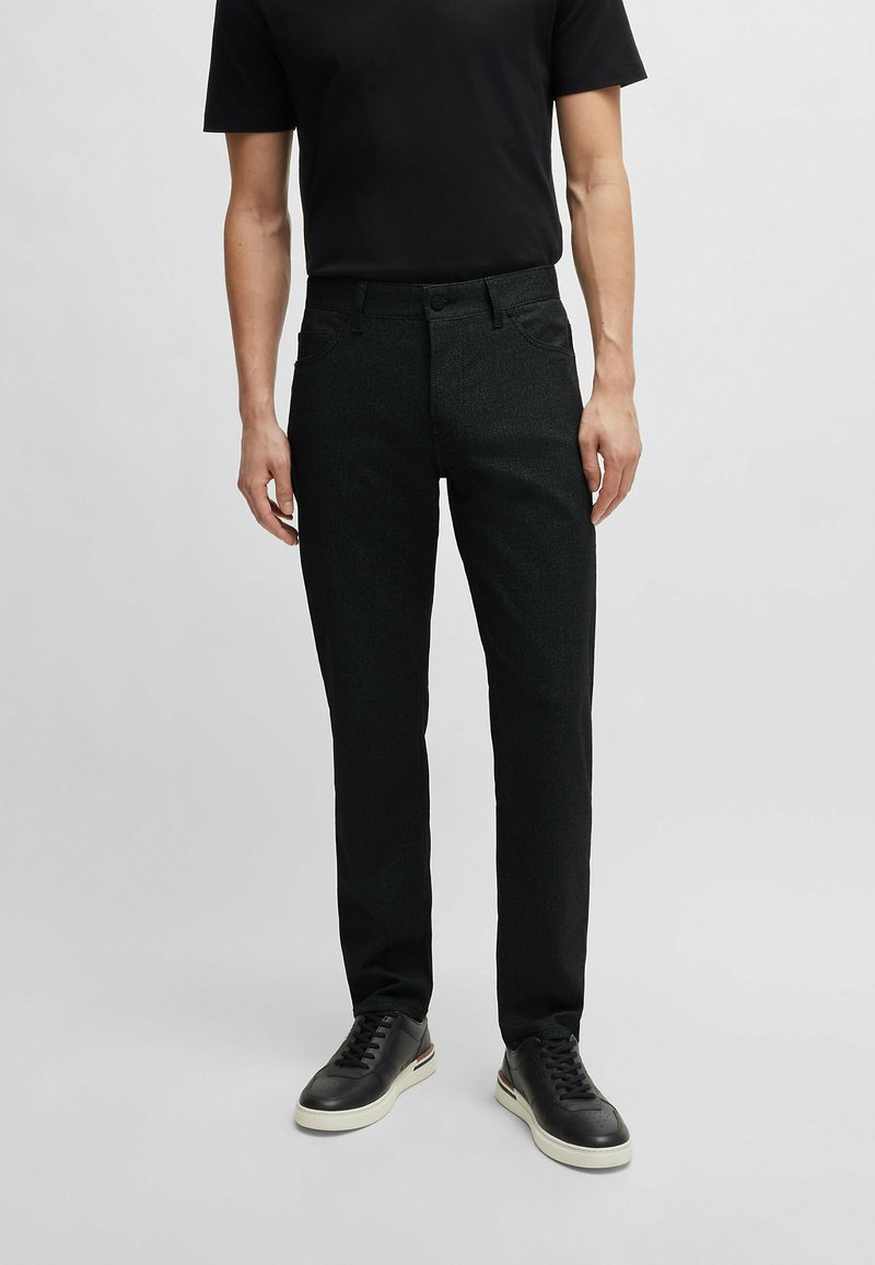 Pantalon slim noir en tissu texturé, doté de poches traditionnelles, d'une fermeture à bouton et associé à des baskets noires.