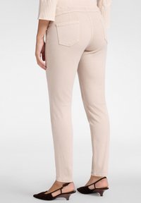 Vaqueros beige de corte slim con una cintura de media altura, bolsillos traseros y una textura suave, combinados con zapatos de tacón oscuros de textura.