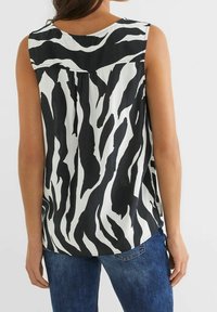 Bezramenný top s černo-bílým zebrovým vzorem, nošený osobou zezadu, v kombinaci s modrými džíny na jednobarevném pozadí.