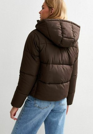 Chaqueta acolchada marrón con capucha, que presenta una textura acolchada y un corte cropped. Combinada con unos jeans de tiro alto en azul claro.