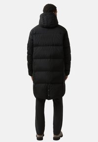 Sort puffermantel med hætte, quiltet design og lang silhuet. Glat tekstur med skjult knaplukning ved kanten.