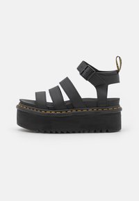 Sandales à plateforme noires avec trois larges lanières, fermeture à boucle et couture jaune sur une semelle épaisse et texturée. Pointe arrondie avec une hauteur de talon.