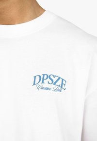 Hvid bomulds t-shirt med et blåt tekstlogo, der læser "DPSZE Creative Labs" i et buet design på venstre brystområde.